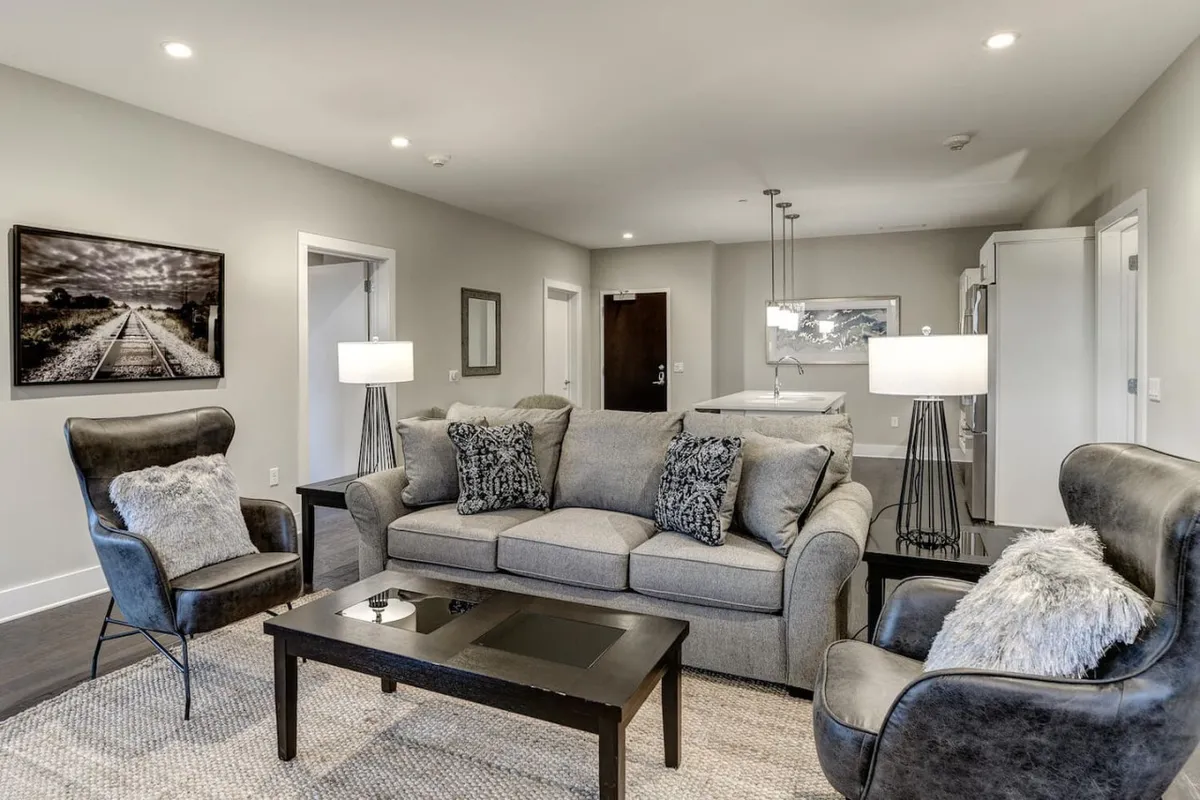 This image displays a stylish living area featuring a comfortable sofa with decorative cushions, a modern coffee table, tasteful wall art, and soft lighting from floor lamps. The setting feels both refined and welcoming, suggesting a space ideal for unwinding or catching up on work in-between meetings.