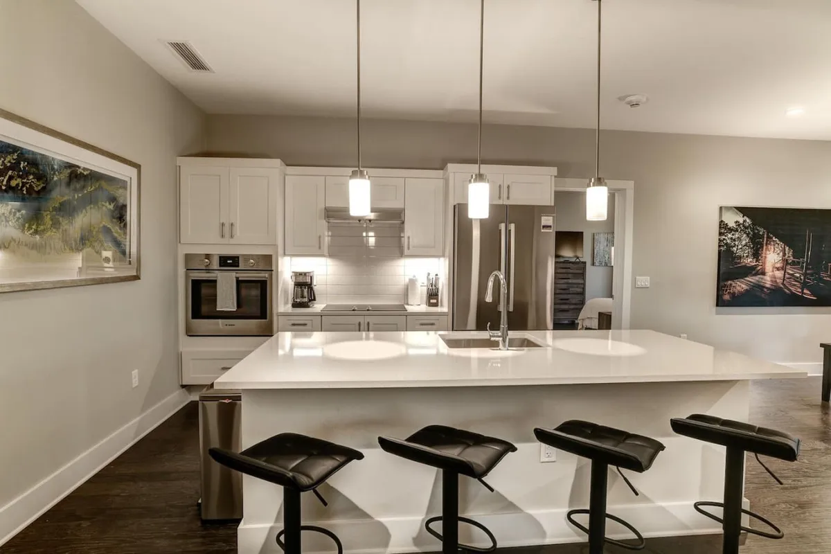 A modern kitchen with an island countertop, bar stools, high-end appliances, and vibrant framed artwork. The setup encourages gatherings for meals, morning coffee, or planning the next day’s exploration.