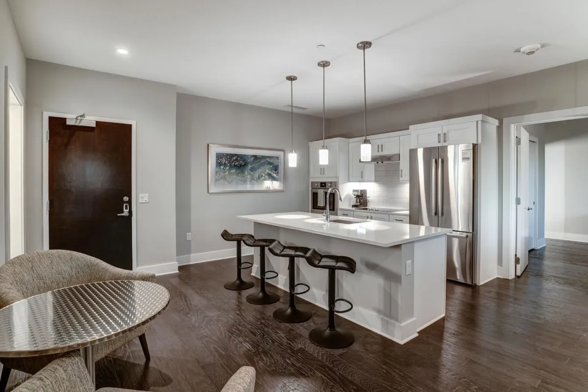 A modern kitchen space with a sleek island and bar stools, accented by contemporary wall art. The design encourages both casual dining and social gatherings, seamlessly connecting to the living area. The open layout keeps guests engaged whether preparing a meal or sharing coffee.