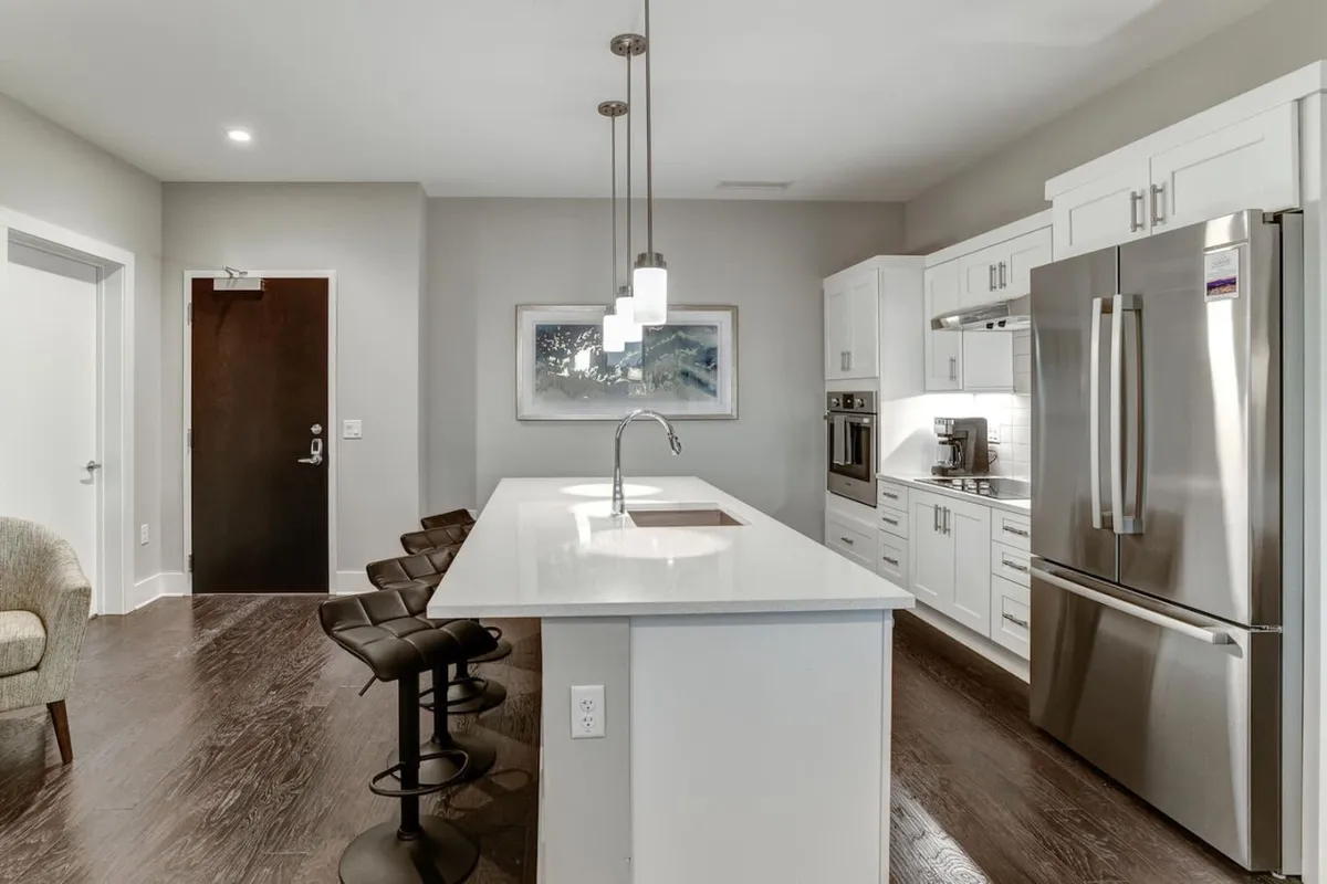 A stylish, contemporary kitchen with an island countertop, bar stools, stainless steel appliances, and vibrant wall art. The space feels open and functional, reflecting a modern urban lifestyle.