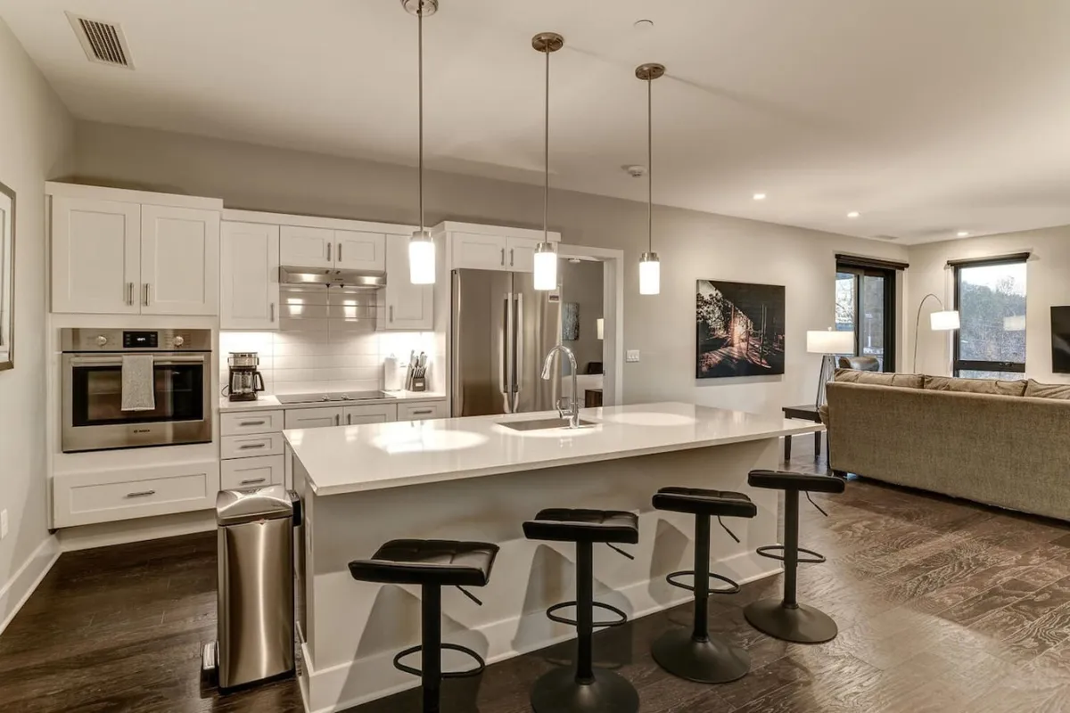 A modern kitchen featuring a spacious island with bar stools, stainless steel appliances, and vibrant artwork on the wall. The setting is arranged for socializing and casual entertaining, suggesting shared meals and lively gatherings.