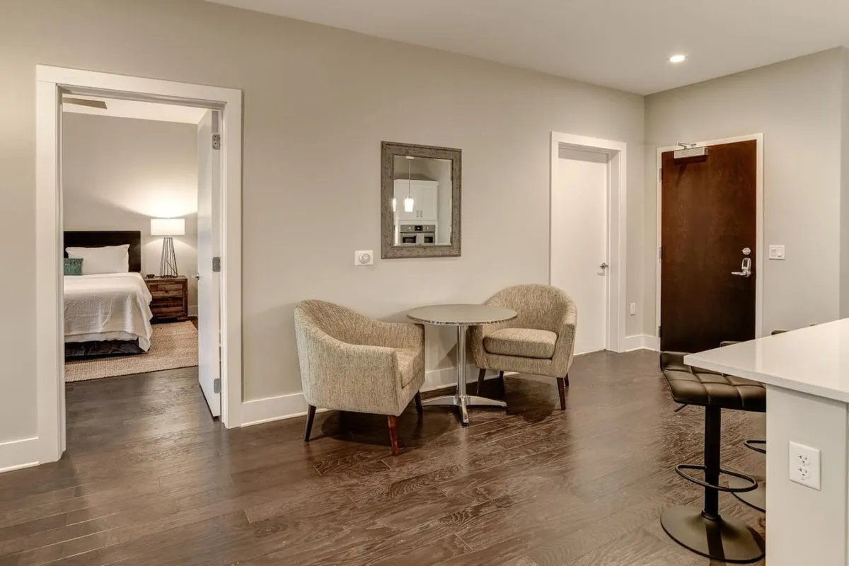 A cozy, modern seating area with a table, chairs, a decorative mirror, and a doorway leading further into the residence. The scene feels inviting, suggesting a comfortable arrival and transition from public to private space.