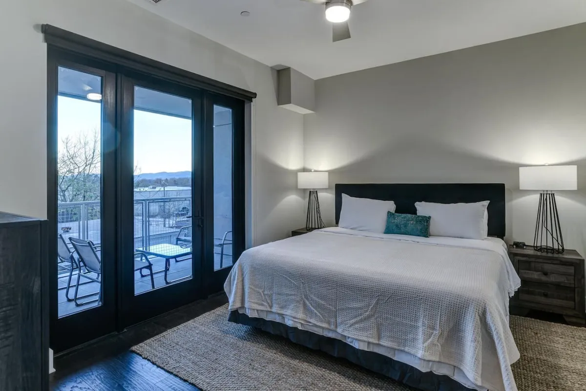 A cozy bedroom with a king bed, luxurious linens, nightstands, soft lighting, and a door leading directly to a private balcony. The space feels inviting and restful, ideal for unwinding after a day of mountain adventures.